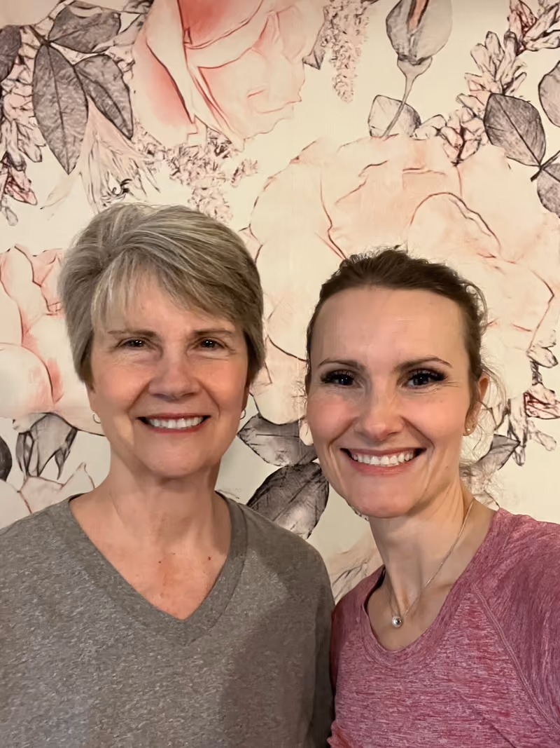 Laurie, left, and her daughter Jayse, smiling in front of a pink floral wall
